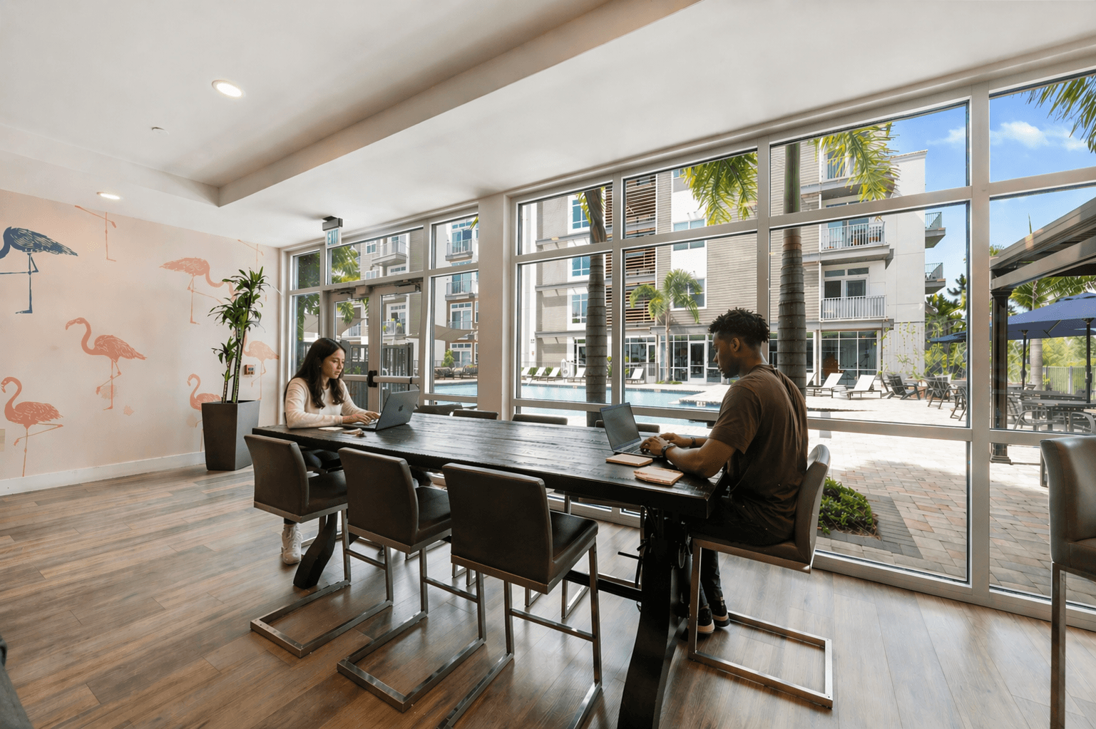Two people working on laptops in a room with a wall mural of flamingos.